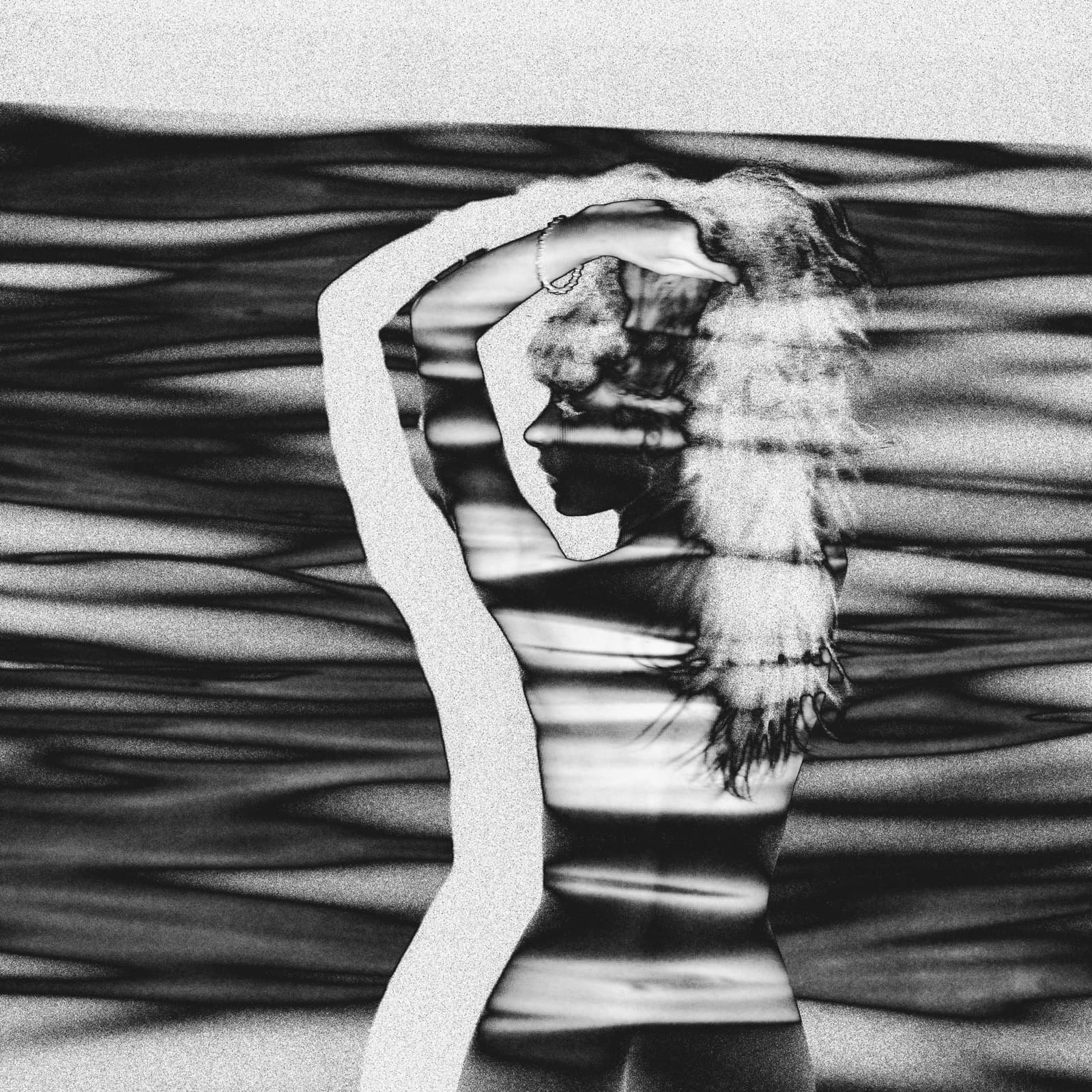 A black and white photograph of a person seen from the back and side, with their arms raised behind their head. A projector light creates a pattern of horizontal bands across the subject's skin and hair, creating a high-contrast solarised effect against a dark, textured background.